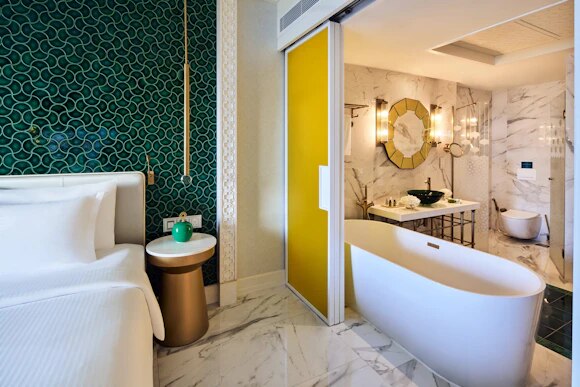 Suite interior with emerald tiled wall, white bed and marble bathroom with freestanding tub